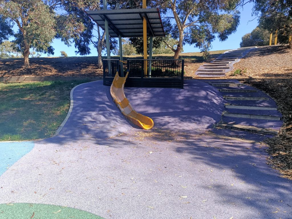 Yellow slide set in a hill side with steps.